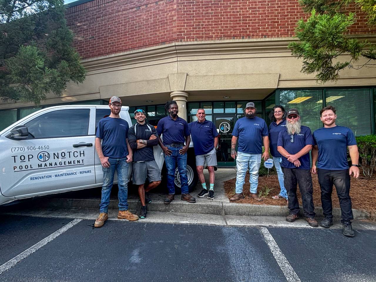 Top Notch Pool Management team standing together in front of company truck and office.