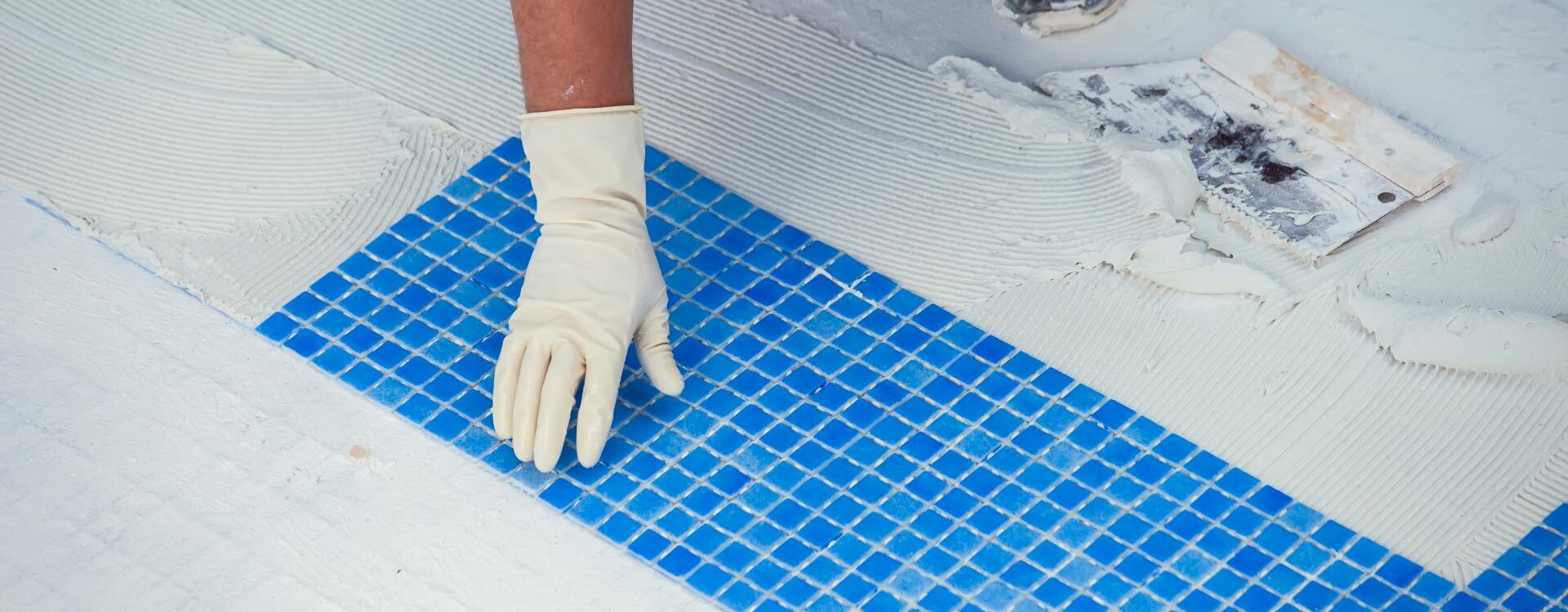 Pool technician installing bright blue mosaic tiles on a pool surface with white mortar during a professional pool repair