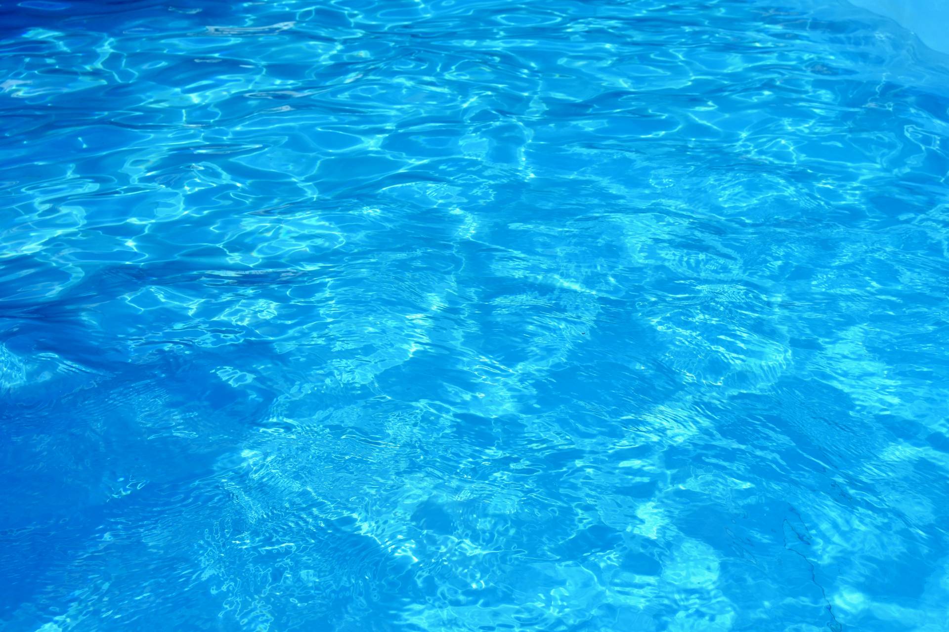 Close-up view of clear blue pool water with sunlight reflections and ripples.