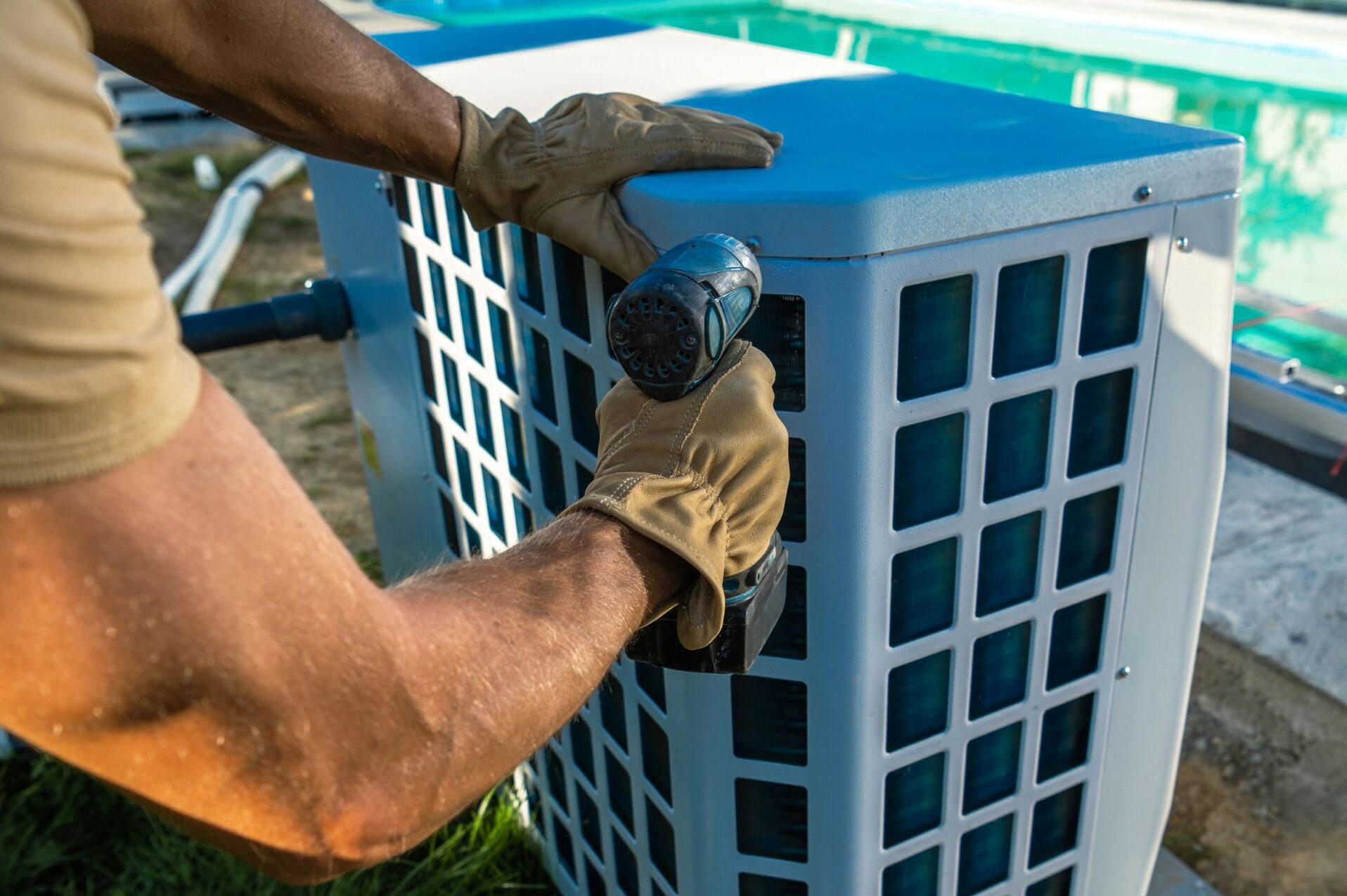 Certified pool technician repairing an outdoor pool heat pump with a power drill beside a residential swimming pool in Atlanta