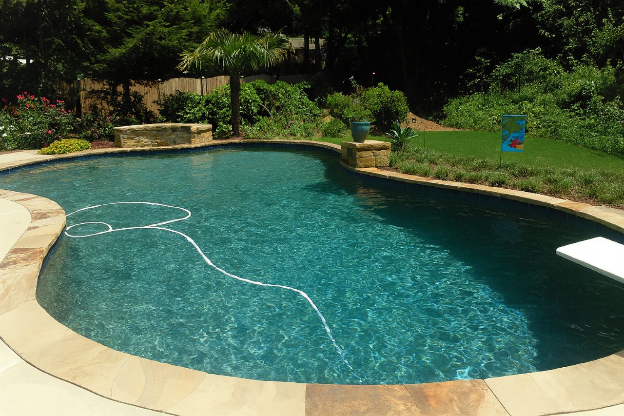 Backyard swimming pool with clear blue water and no waterfalls or fountains, surrounded by stone coping and landscaping.