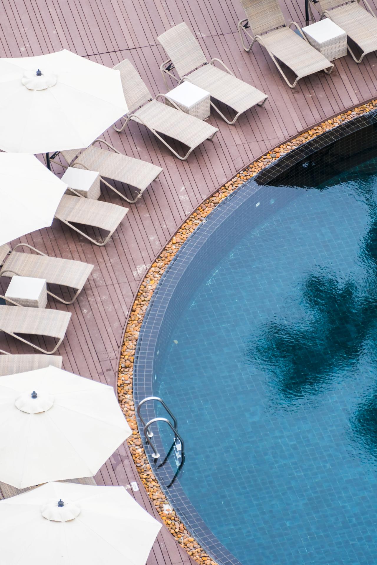 Overhead view of a clean community swimming pool with lounge chairs, umbrellas, wood decking, and clear blue water at a residential HOA property.